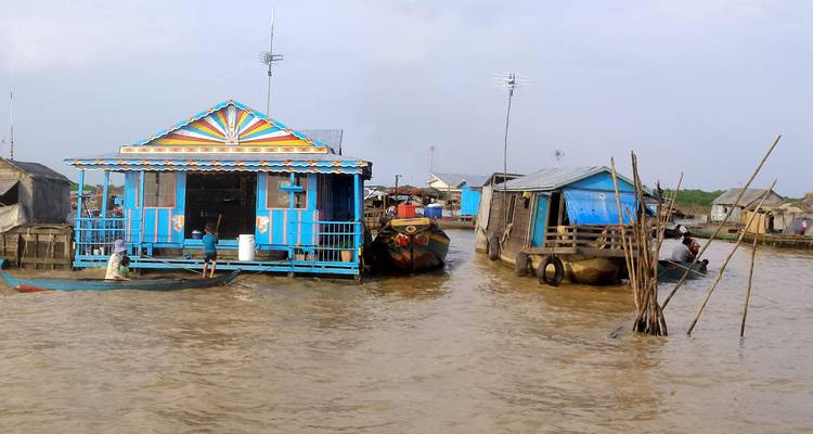 Brightly painted floating houses and boats rest on muddy waters of a riverside village.