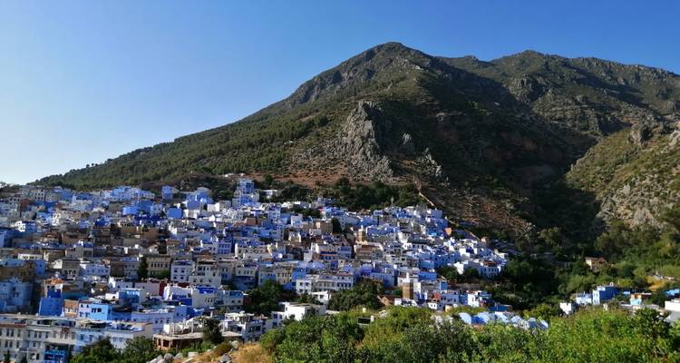 Blauw geschilderd stadje met bergachtergrond op een heldere dag.
