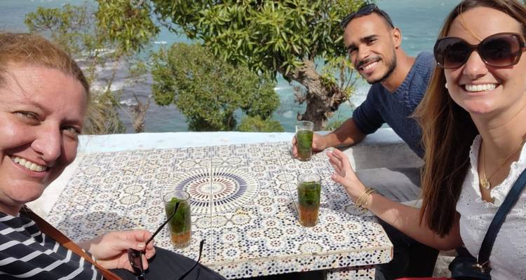 Drie mensen genieten van drankjes aan een decoratieve tafel met uitzicht op zee.