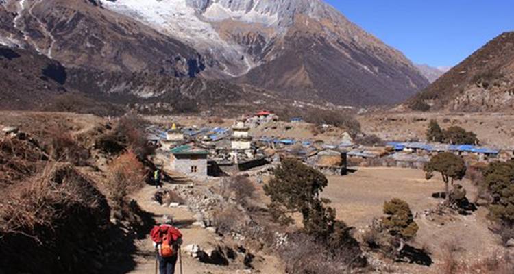 Wanderer nähern sich einem Himalaya-Dorf mit einer Bergkulisse.