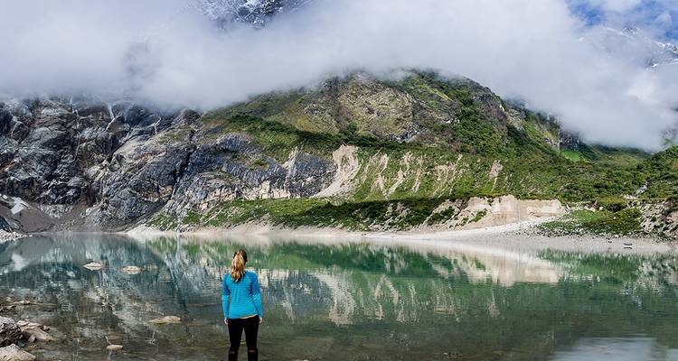 Person an einem ruhigen See mit Bergen im Hintergrund.