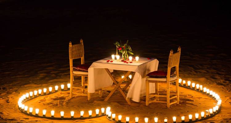 Romantische kaarsverlichting dinersetup met twee stoelen omringd door lantaarns op woestijnzand onder de nachtelijke hemel.