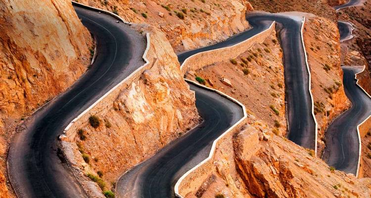 Luchtfoto van een slangenachtig geasfalteerde weg die zich kronkelt door steile oranje canyonwanden.