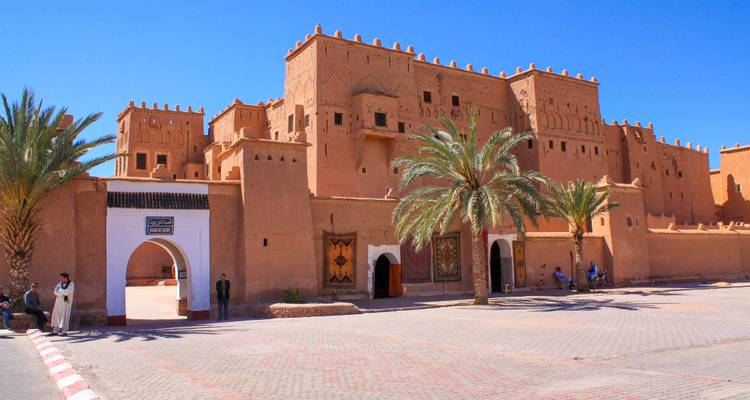 Aarden Kasbah Taourirt in Ouarzazate omringd door palmbomen onder een stralend blauwe hemel.