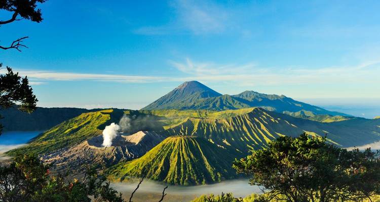 Vue spectaculaire du lever de soleil sur le cratère fumant du mont Bromo et la caldeira ridée environnante sous un ciel bleu.