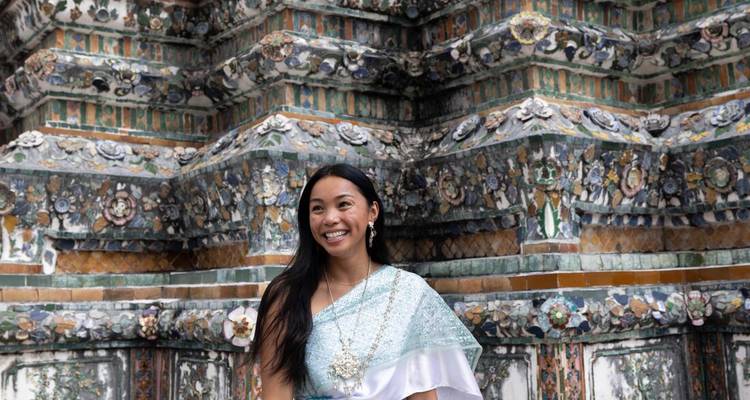 Femme en élégante robe thaïlandaise pose et sourit devant les carreaux floraux complexes du mur d'un temple historique.