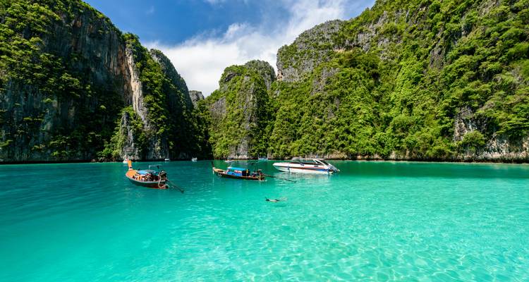 Lagon turquoise entouré de falaises calcaires imposantes avec des bateaux à longue queue et un plongeur avec tuba flottant dans une eau claire.