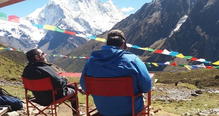 Deux personnes assises à l'extérieur avec des drapeaux de prière et des montagnes enneigées en arrière-plan