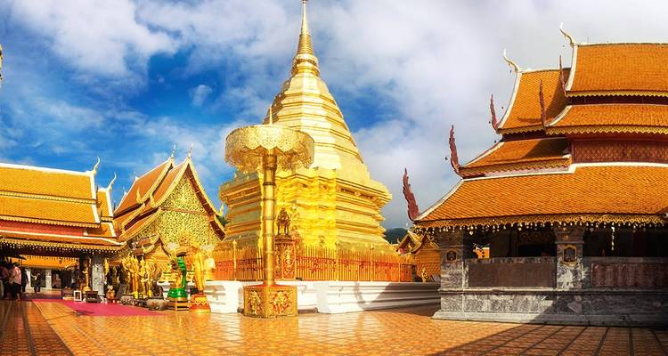La estupa de oro con espiras y los templos ornamentados de Wat Phra That Doi Suthep brillan bajo un cielo azul vivido.