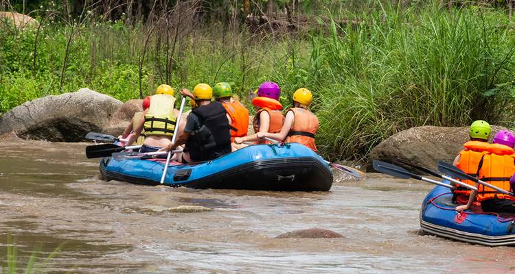 Dos balsas inflables con remeros con casco flotan por un río de la jungla fangoso listos para la acción de aguas blancas.