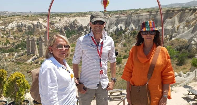 Three people posing with a hot air balloon in a scenic rocky landscape.
