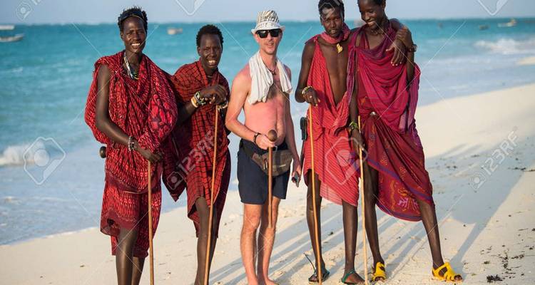 A man posing with local tribesmen on a beach.