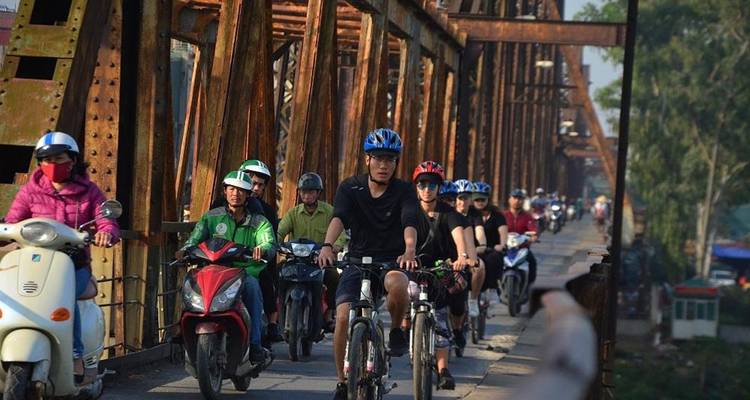 Groupe de personnes à vélo et en scooter sur un pont.