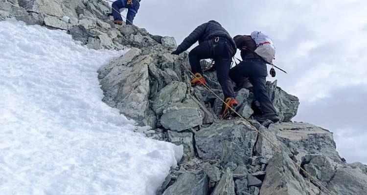 Bergsteiger, die einen felsigen und verschneiten Bergpfad hinaufsteigen.