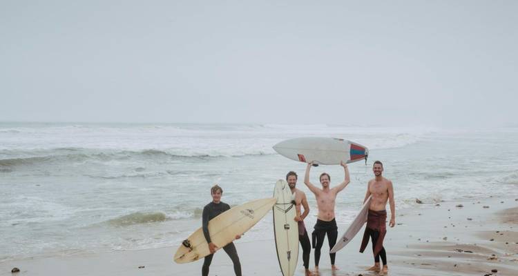 Grupo de surfistas sosteniendo tablas de surf en una playa nublada.