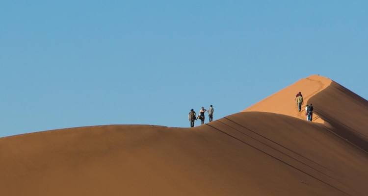 Personas caminando sobre una duna de arena en un desierto.