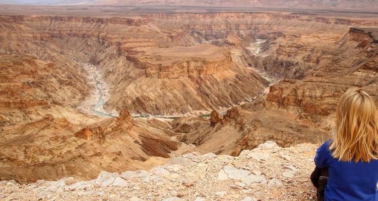 Persona sentada cerca del borde de un vasto cañón.