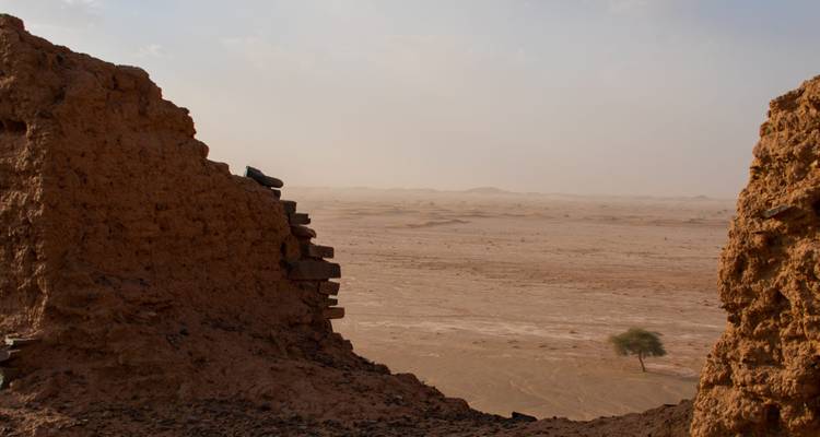 Uitzicht door afbrokkelende leemwanden over een uitgestrekt, vlak woestijnlandschap onder een nevelige hemel