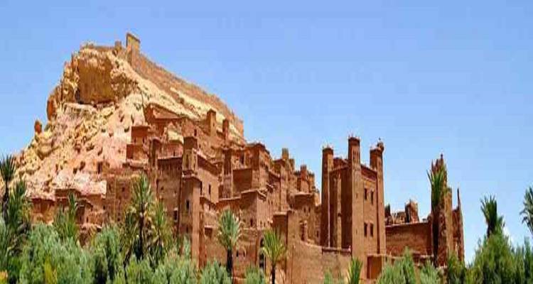 Historisch adobe kasbah-dorp gelegen op een heuvel met palmbomen en een heldere blauwe hemel