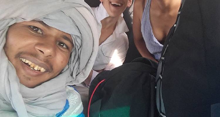 Glimlachende woestijngids in hoofddoek die een selfie maakt met twee reizigers in het voertuig