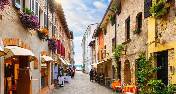Pintoresca calle de adoquines bordeada de tiendas coloridas, cafés y jardineras de flores que conducen al lago