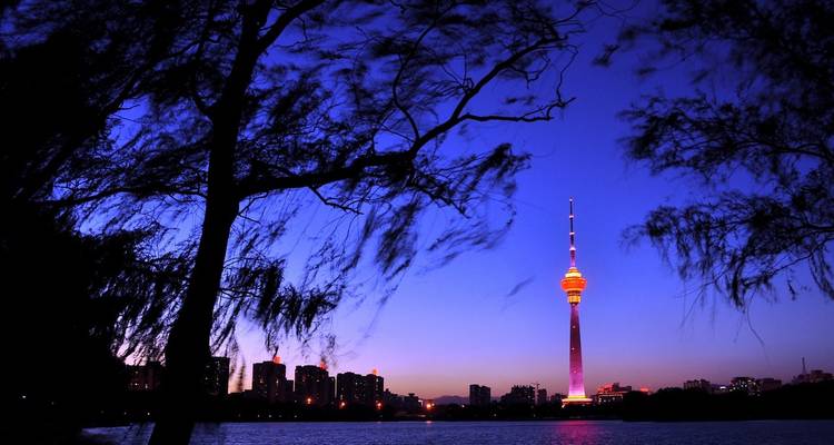 Illuminated TV tower at night reflecting in water.