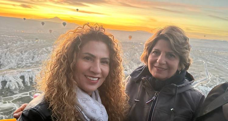 Twee vrouwen die glimlachen met heteluchtballonnen op de achtergrond bij zonsondergang.
