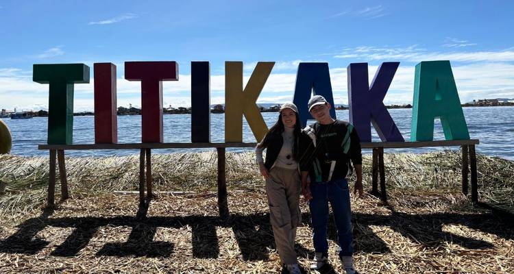 Deux personnes posent devant un grand panneau 'TITIKAKA' au bord d'un lac.