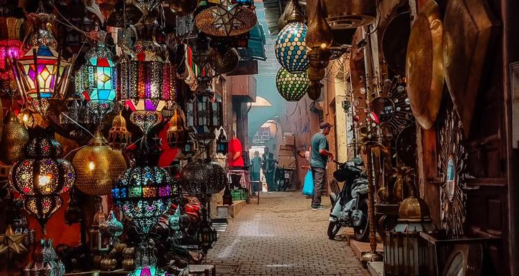 Callejón estrecho iluminado con faroles en el zoco de Marrakech lleno de lámparas de metal coloridas y compradores.