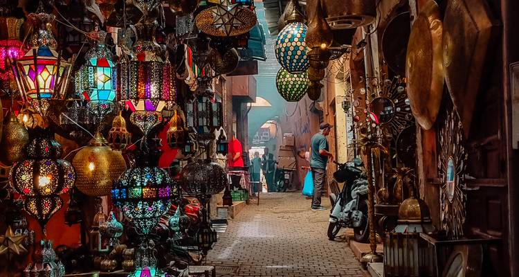Callejón del zoco lleno de faroles con lámparas colgantes vibrantes y compradores explorando productos tradicionales.