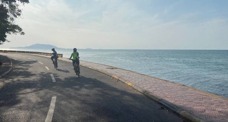 Dos ciclistas en camino junto a una carretera costera.