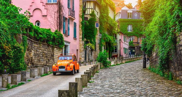 Altes oranges Auto fährt durch eine bunte, schmale Straße in Paris.