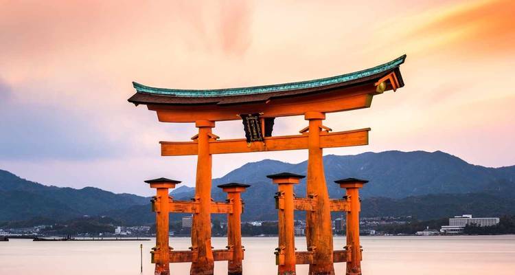Iconische Torii-poort die in het water staat met bergen op de achtergrond.