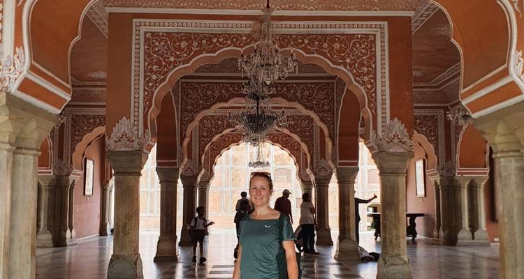 Person standing in an opulent hallway with intricate arches and chandeliers.
