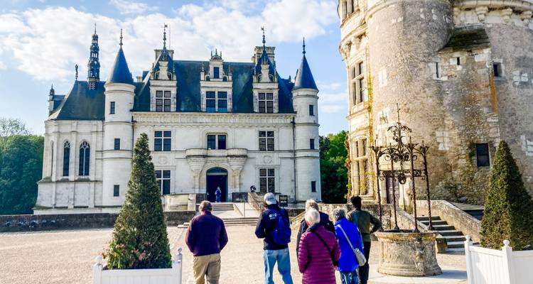 Les visiteurs se tiennent devant la façade grandiose d'un château blanc avec des tours ornées et un puits en pierre au premier plan.