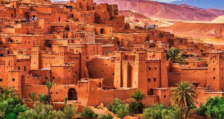 Estructuras históricas de adobe de la kasbah de Ait Benhaddou brillando con luz cálida con palmeras abajo