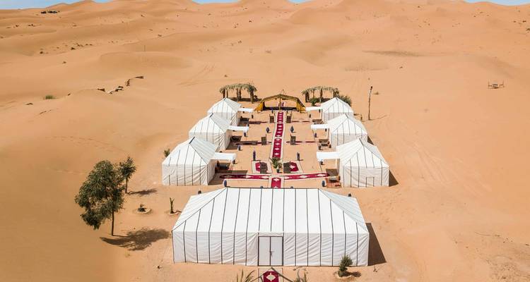 Campamento de lujo en el desierto con tiendas blancas alineadas y alfombras rojas en las dunas de Erg Chebbi