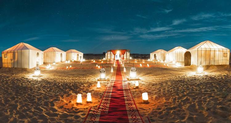 Vista nocturna de tiendas de campamento del desierto iluminadas bajo un cielo estrellado con pasarela de alfombra roja