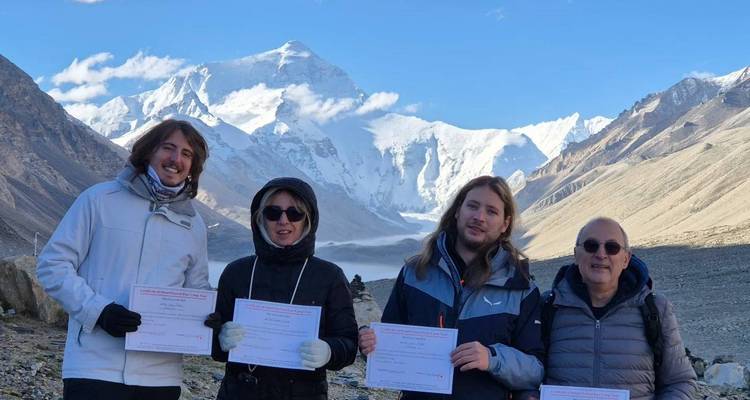 Cuatro trekistas sosteniendo certificados en un mirador con la cara norte nevada del Monte Everest elevándose detrás de ellos.