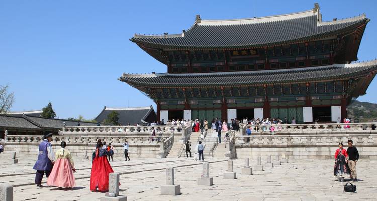 Visitantes con hanbok explorando el amplio patio de un gran palacio coreano
