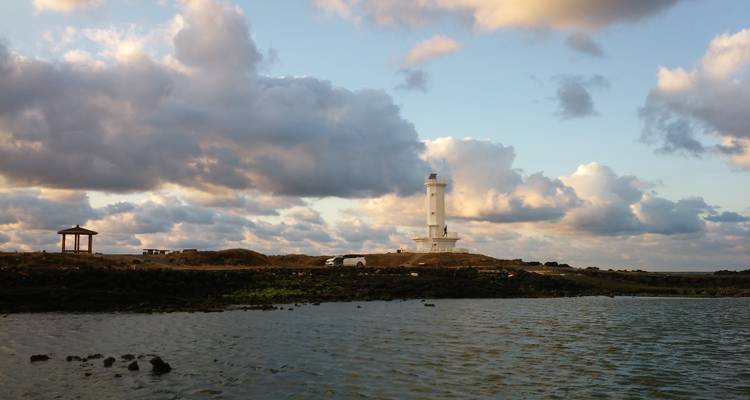 El faro blanco se alza en una costa azotada por el viento de Jeju-do bajo un cielo lleno de nubes dramáticas.