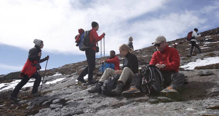 Groupe de randonneurs se reposant sur une pente rocheuse avec des montagnes enneigées en arrière-plan.