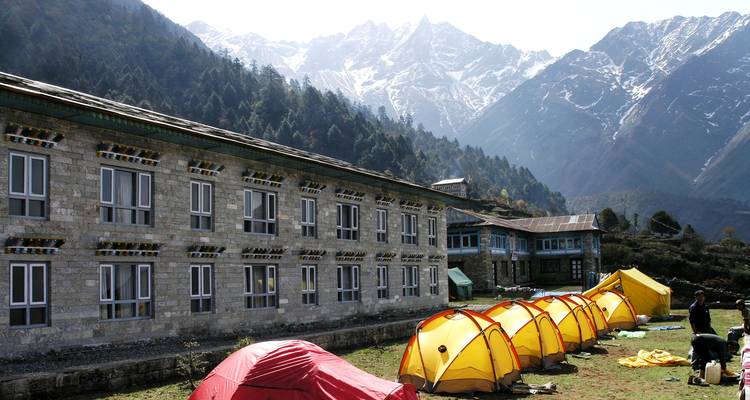 Tentes installées devant des refuges de montagne avec des falaises boisées et des montagnes en arrière-plan.