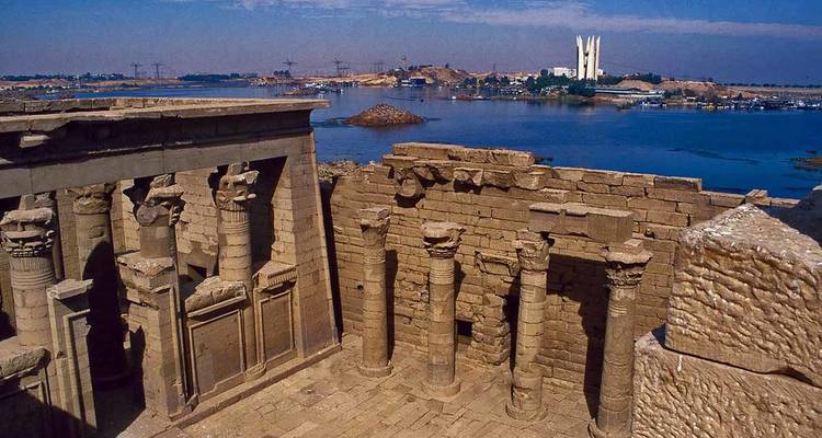 Ancient Egyptian ruins with a river and city in the background.