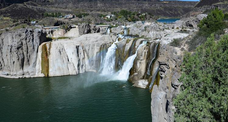 Breiter Wasserfall, der in einem felsigen Landschaftsbild in einen Fluss stürzt.