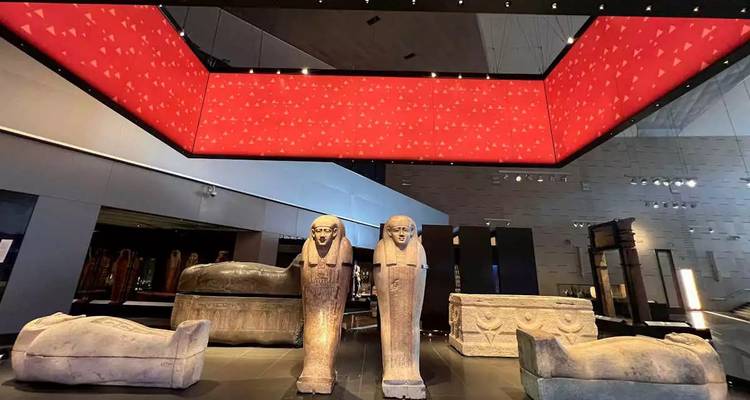 Tentoonstelling van antieke stenen sarcofagen in een moderne museumomgeving.