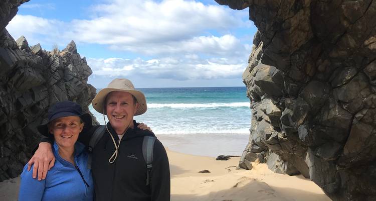 Couple standing near a rocky beach entrance with the ocean in the background.