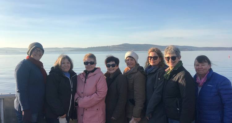 Group of people standing on a boat with a calm water backdrop.