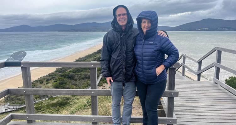 Couple standing on a wooden platform with a beach and ocean view.