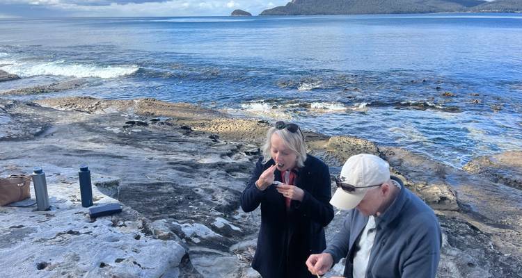 Two people sitting by the rocky shore enjoying the ocean view.